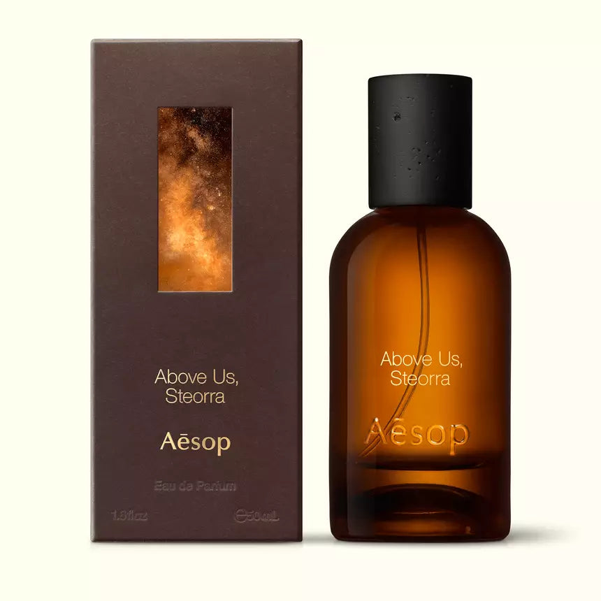 Amber glass Aesop Above Us, Steorra Eau de Parfum bottle beside its brown outer box on a white background.