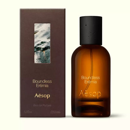 Amber glass Aesop Boundless Eremia Eau de Parfum bottle beside its brown outer box on a white background.