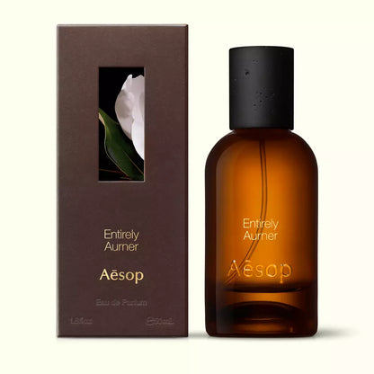 Amber glass Aesop Entirely Aurner Eau de Parfum bottle beside its brown outer box on a white background.