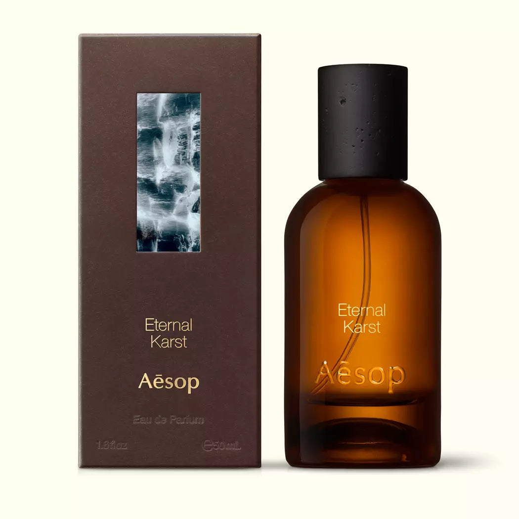 Amber glass Aesop Eternal Karst Eau de Parfum bottle beside its brown outer box on a white background.