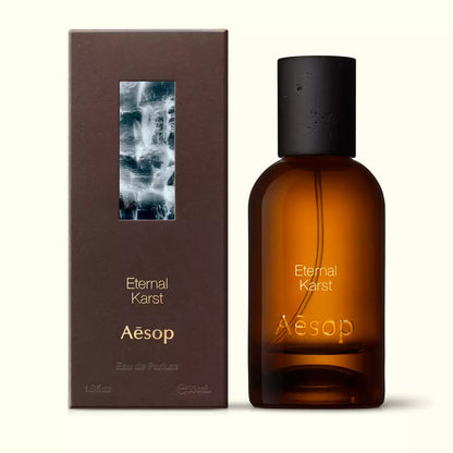 Amber glass Aesop Eternal Karst Eau de Parfum bottle beside its brown outer box on a white background.