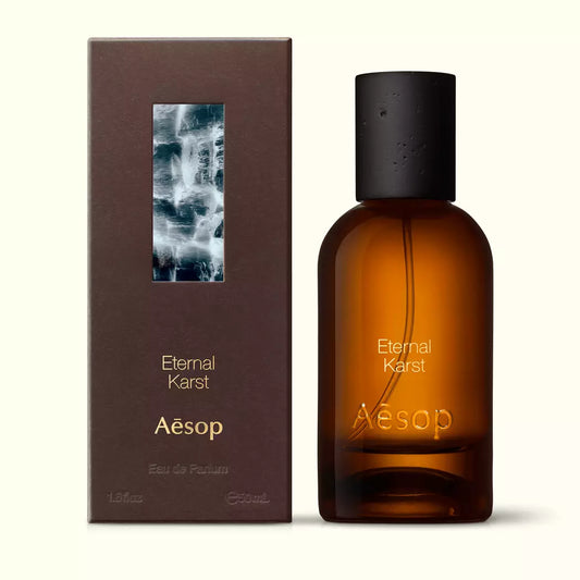 Amber glass Aesop Eternal Karst Eau de Parfum bottle beside its brown outer box on a white background.