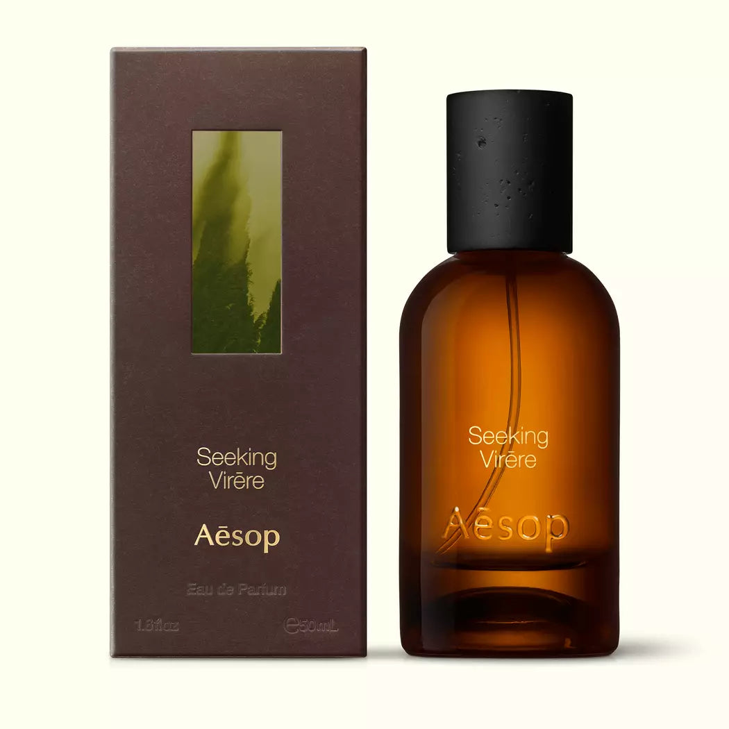 Amber glass Aesop Seeking Virere Eau de Parfum bottle beside its brown outer box on a white background.