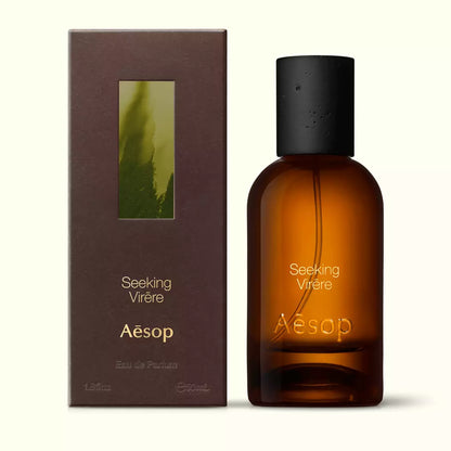 Amber glass Aesop Seeking Virere Eau de Parfum bottle beside its brown outer box on a white background.