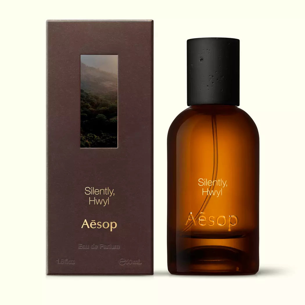 Amber glass Aesop Silently Hwyl Eau de Parfum bottle beside its brown outer box on a white background.