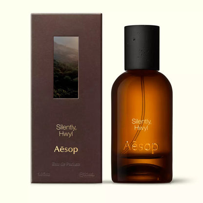 Amber glass Aesop Silently Hwyl Eau de Parfum bottle beside its brown outer box on a white background.