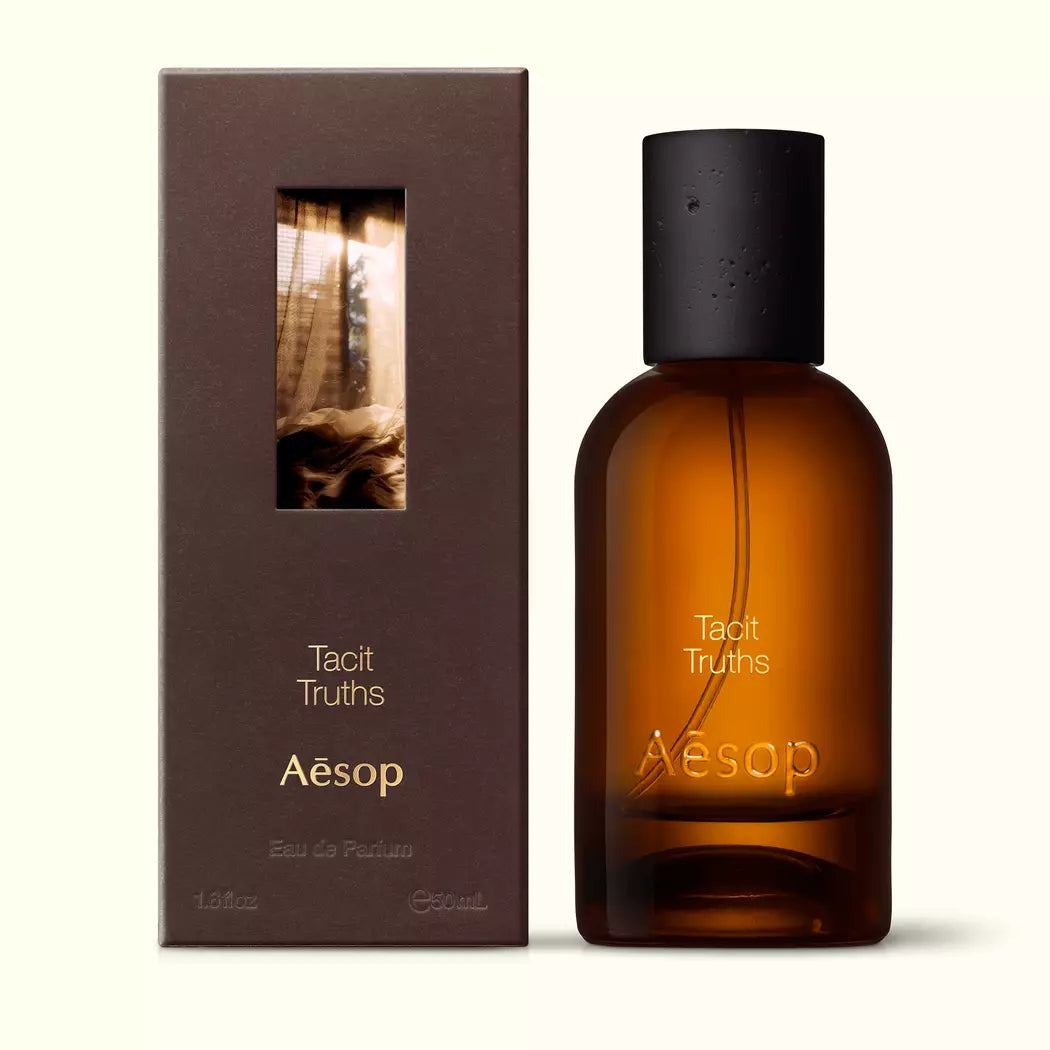 Amber glass Aesop Tacit Truths Eau de Parfum bottle beside its brown outer box on a white background.