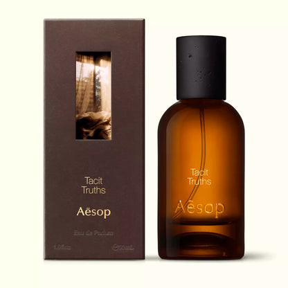 Amber glass Aesop Tacit Truths Eau de Parfum bottle beside its brown outer box on a white background.