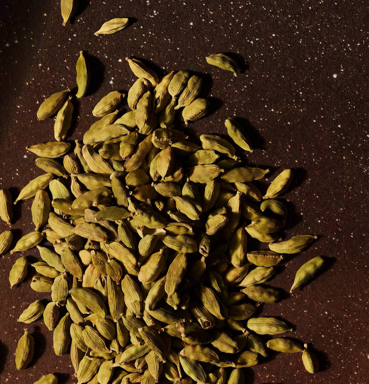 Close-up of green cardamom pods scattered across a dark surface.