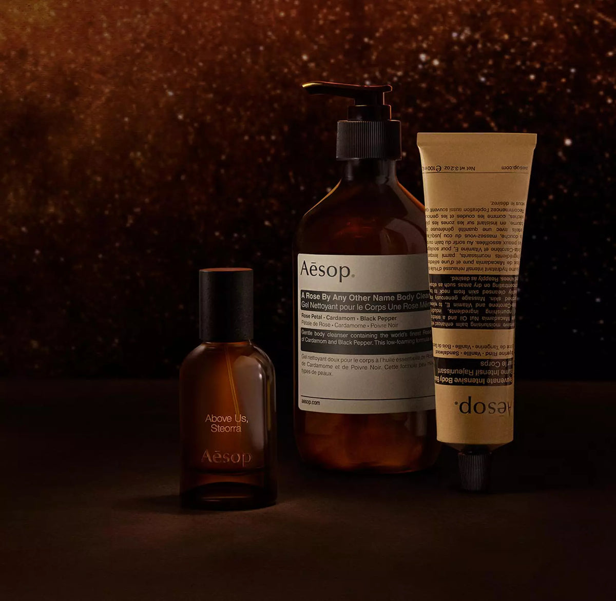 Aesop Above Us, Steorra bottle with pump bottle and tube against a warm speckled brown backdrop.