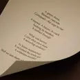 Curved cream page with printed verse against a dark brown background.