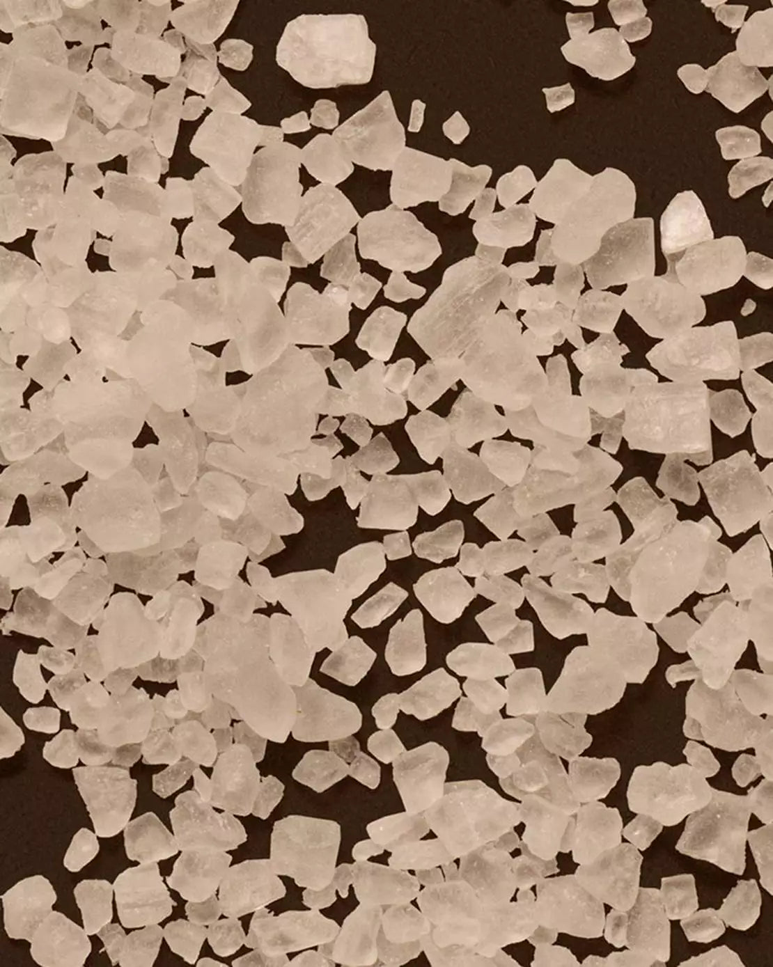 Close-up of coarse white salt crystals scattered across a dark surface.