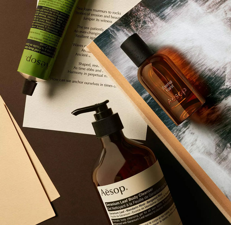 Aesop Eternal Karst bottle with pump bottle and green tube arranged on papers with foaming water imagery.
