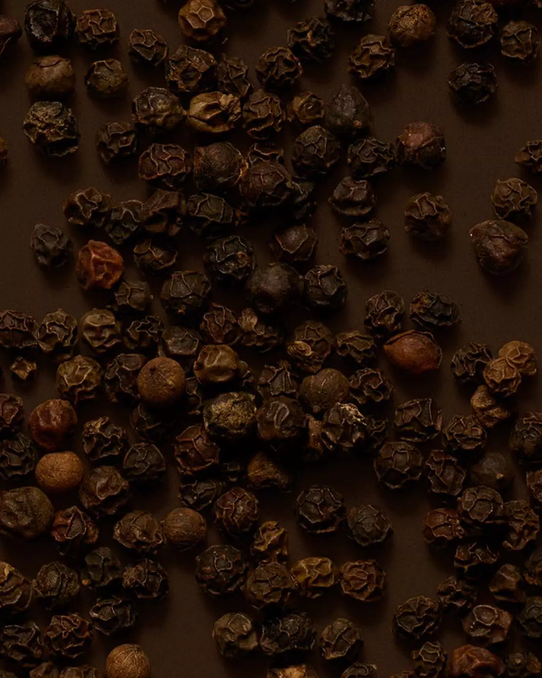Close-up of peppercorns scattered across a dark brown surface.
