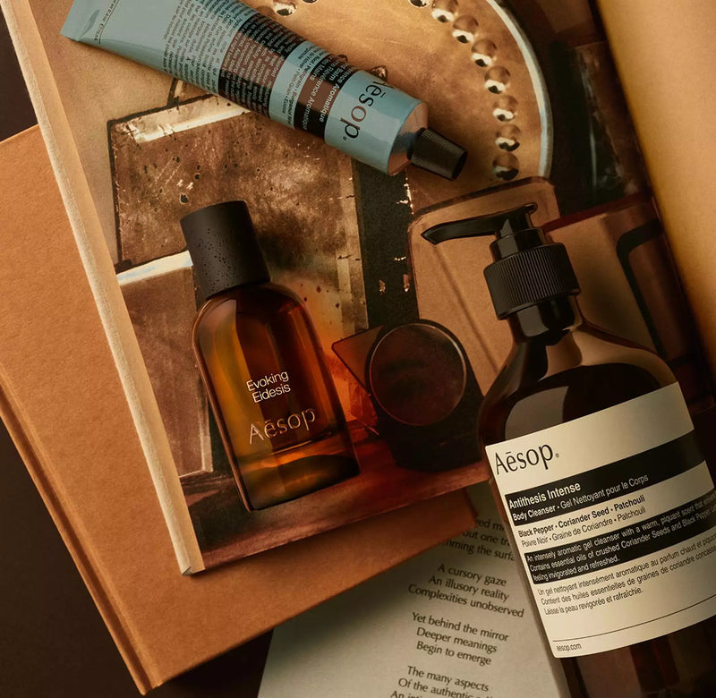 Aesop Evoking Eidesis bottle with pump bottle and blue tube arranged on papers and mirrored tray imagery.