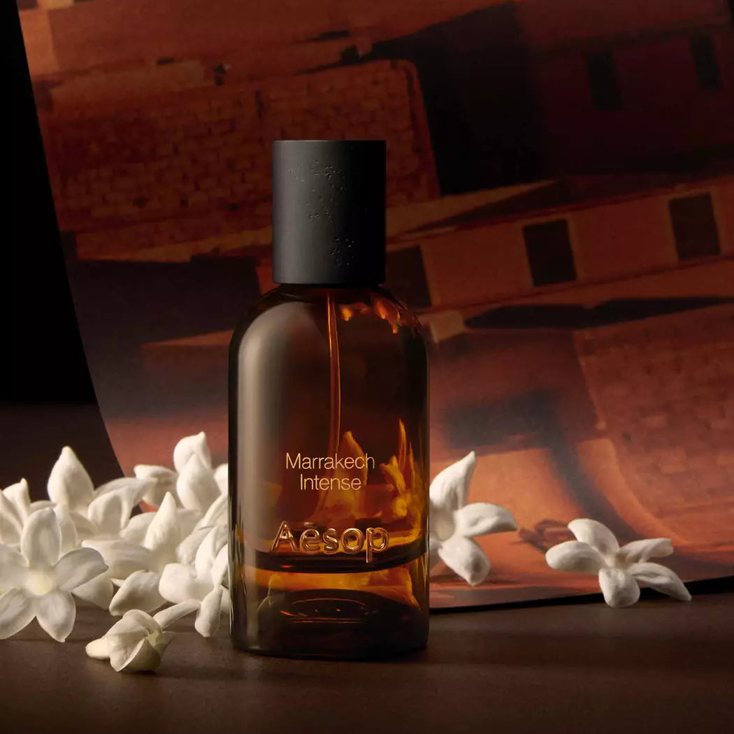 Aesop Marrakech Intense bottle with white flowers and an architectural backdrop.