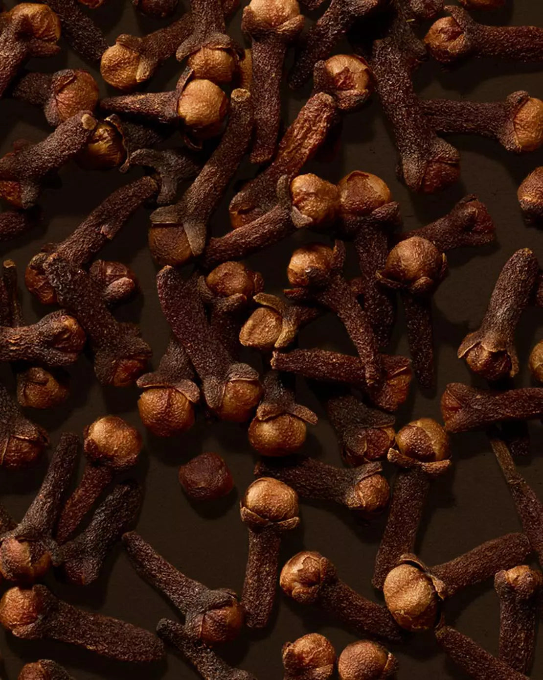 Close-up of cloves scattered across a dark brown surface.