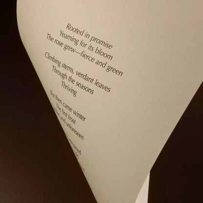 Curved cream page with printed verse against a dark brown background.