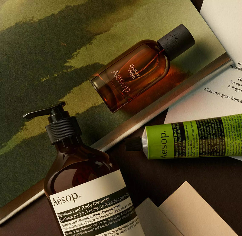 Aesop Seeking Virere bottle with pump bottle and green tube arranged on papers with painted green imagery.