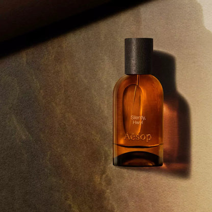 Aesop Silently Hwyl bottle in sunlight against a warm brown background.