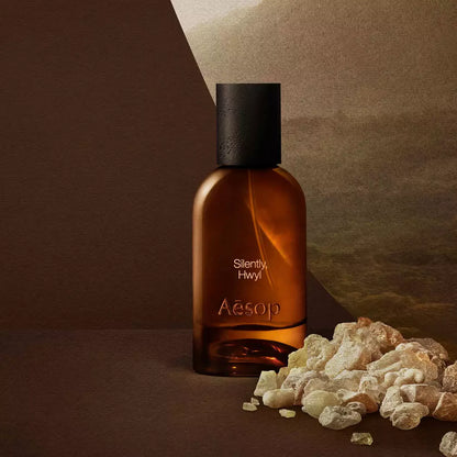 Aesop Silently Hwyl bottle beside resin stones on a dark surface.