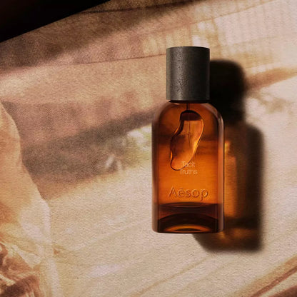 Aesop Tacit Truths bottle on draped fabric in warm sunlight.