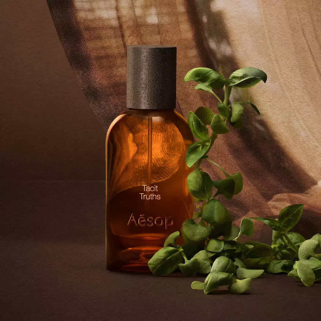 Aesop Tacit Truths bottle with basil sprigs against warm fabric.