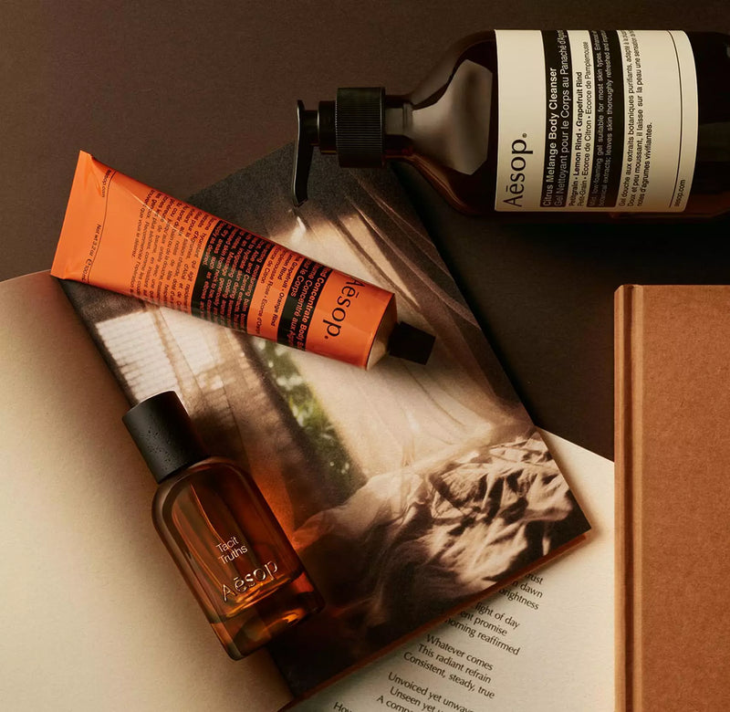 Aesop Tacit Truths bottle with pump bottle and orange tube arranged on papers with a monochrome image.